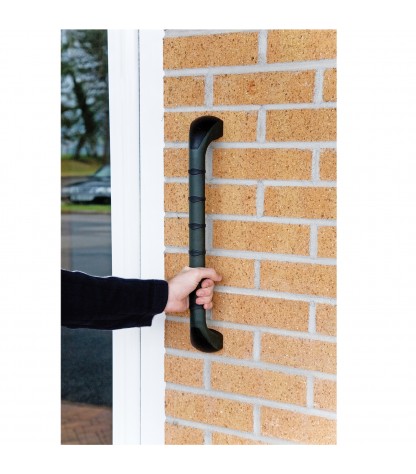 Main saisissant la barre d'appui extérieure PRIMA 46 cm noire fixée sur façade en brique près d'une porte d'entrée