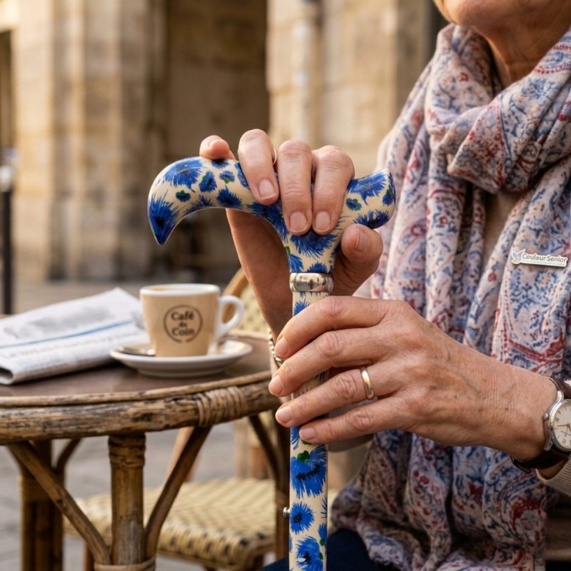 Poignée ergonomique Derby fleurie bleuets , tenue par une femme de 60 ans, avec canne de marche chic.