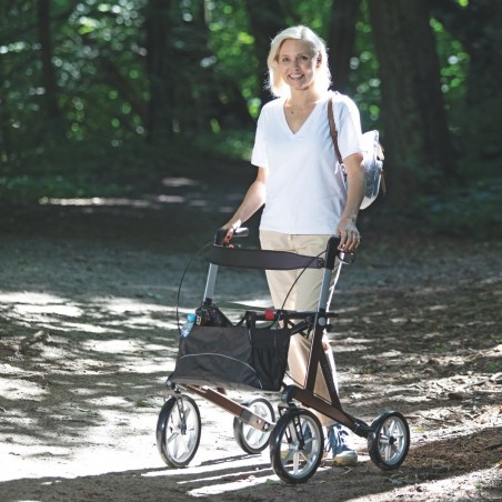 Senior actif marchant en forêt avec son rollator tout-terrain à 4 roues, robuste et doté d'une structure rigide.