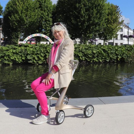 Femme assise et souriante avec déambulateur 4 roues Carbon Ultralight ACRE or champagne