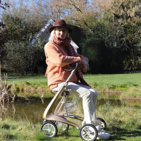 femme senior qui se repose assise avec le déambulateur 4 roues Carbon Ultralight ACRE or champagne