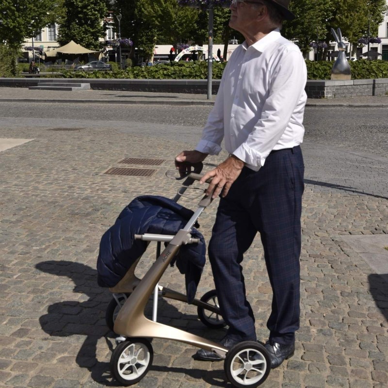 Homme senior qui se déplace avec son déambulateur 4 roues Carbon Ultralight ACRE or champagne