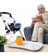 Senior assis lisant un livre avec un déambulateur Neo Indoor blanc et son plateau amovible posé, très pratique pour l’intérieur.