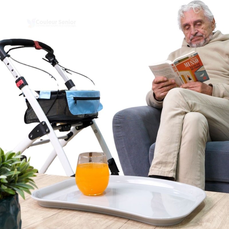 Senior assis lisant un livre avec un déambulateur Neo Indoor blanc et son plateau amovible posé, très pratique pour l’intérieur.