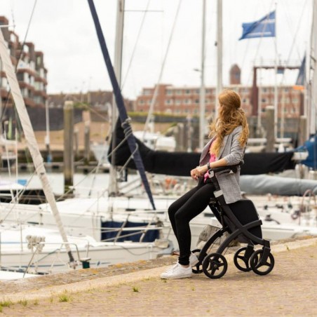 Femme assise sur le siège du rollator Rollz Flex noir au bord d'un port de plaisance