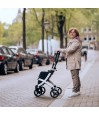 Senior debout dans une rue pavée tenant le rollator Rollz Flex blanc replié et compact
