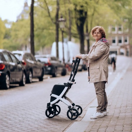 Senior debout dans une rue pavée tenant le rollator Rollz Flex blanc replié et compact