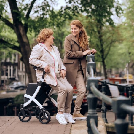 Senior assise sur rollator Rollz Flex blanc discutant avec une jeune femme au bord d'un canal