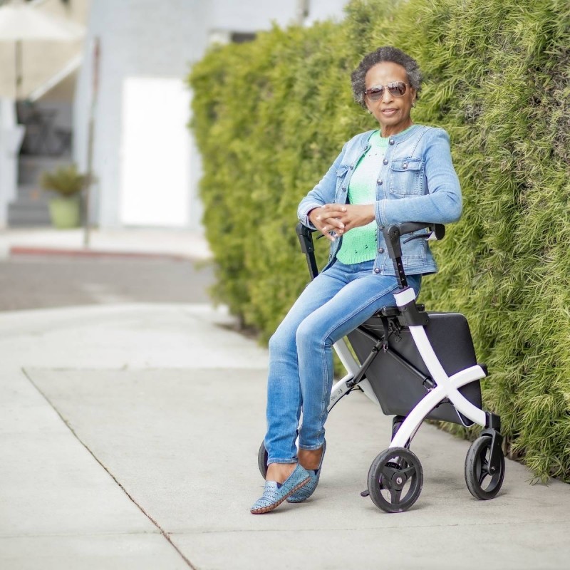 Dame élégante assise sur le siège du rollator Rollz Flex blanc en extérieur, détendue