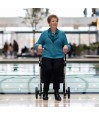 Senior souriante tenant le rollator Rollz Flex blanc dans un grand centre commercial lumineux