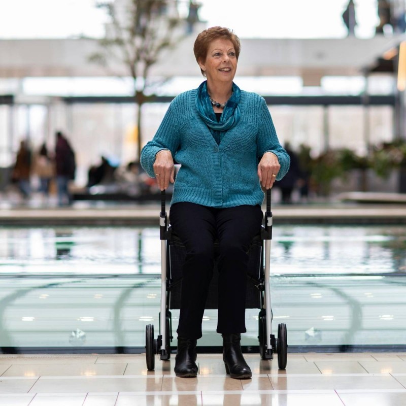 Senior souriante tenant le rollator Rollz Flex blanc dans un grand centre commercial lumineux