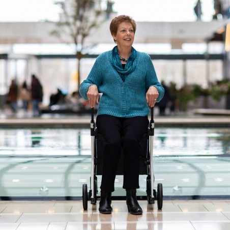 Senior souriante tenant le rollator Rollz Flex blanc dans un grand centre commercial lumineux