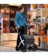 Dame senior poussant rollator caddy Rollz Flex blanc devant une vitrine de maroquinerie