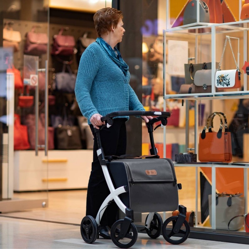 Dame senior poussant rollator caddy Rollz Flex blanc devant une vitrine de maroquinerie