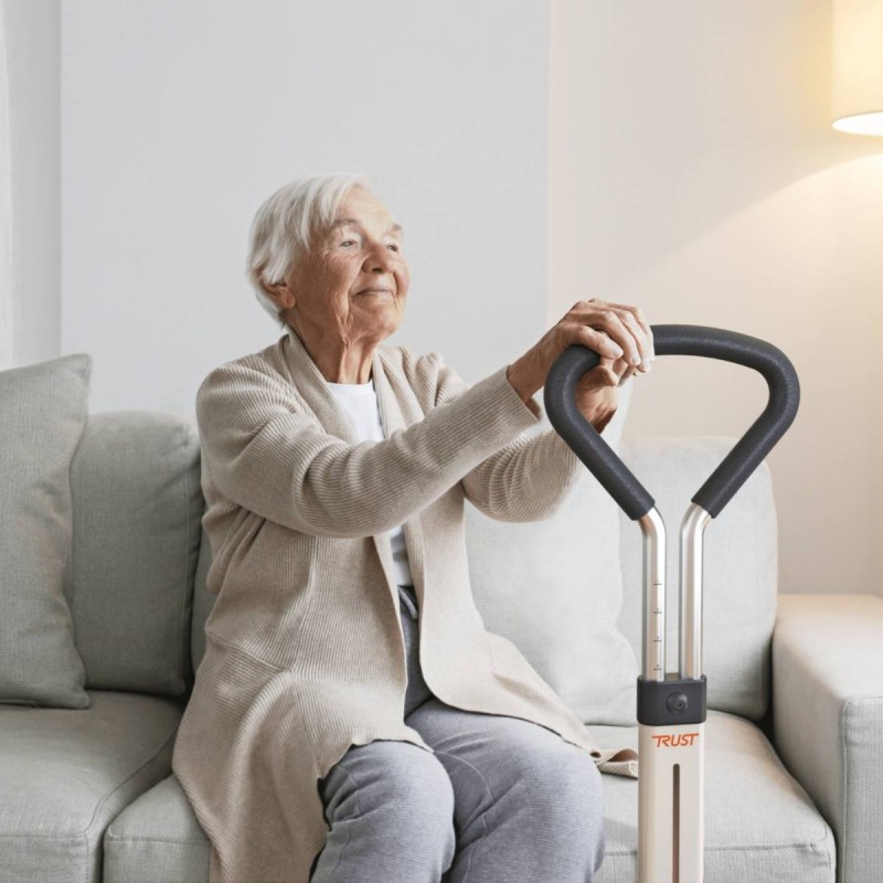 Senior souriante assise sur canape s'appuyant sur poignee Let's Get Up Trustcare blanche