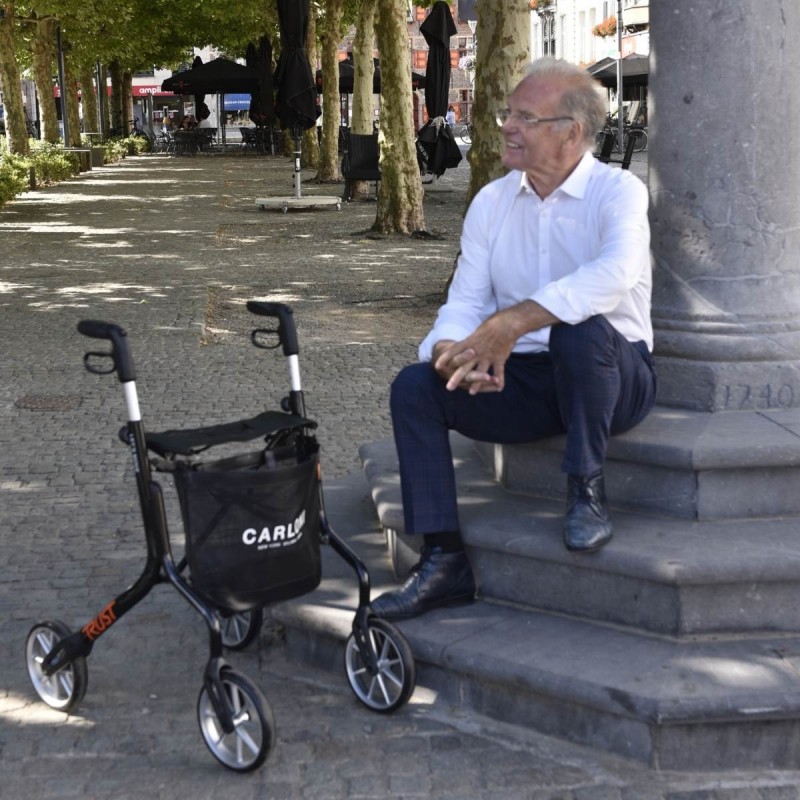 Senior homme assis souriant déambulateur lets move noir sac carloni place publique autonomie