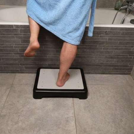 Personne en train de franchir le bord de la baignoire en s'aidant d'un marchepied de sécurité stable